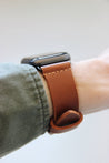 Seitenansicht einer Apple Watch am Handgelenk mit einem Lederband in Braun.