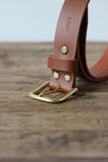 Detailansicht der Schnalle eines Herren Ledergürtel in Braun auf einer Holzplatte.
