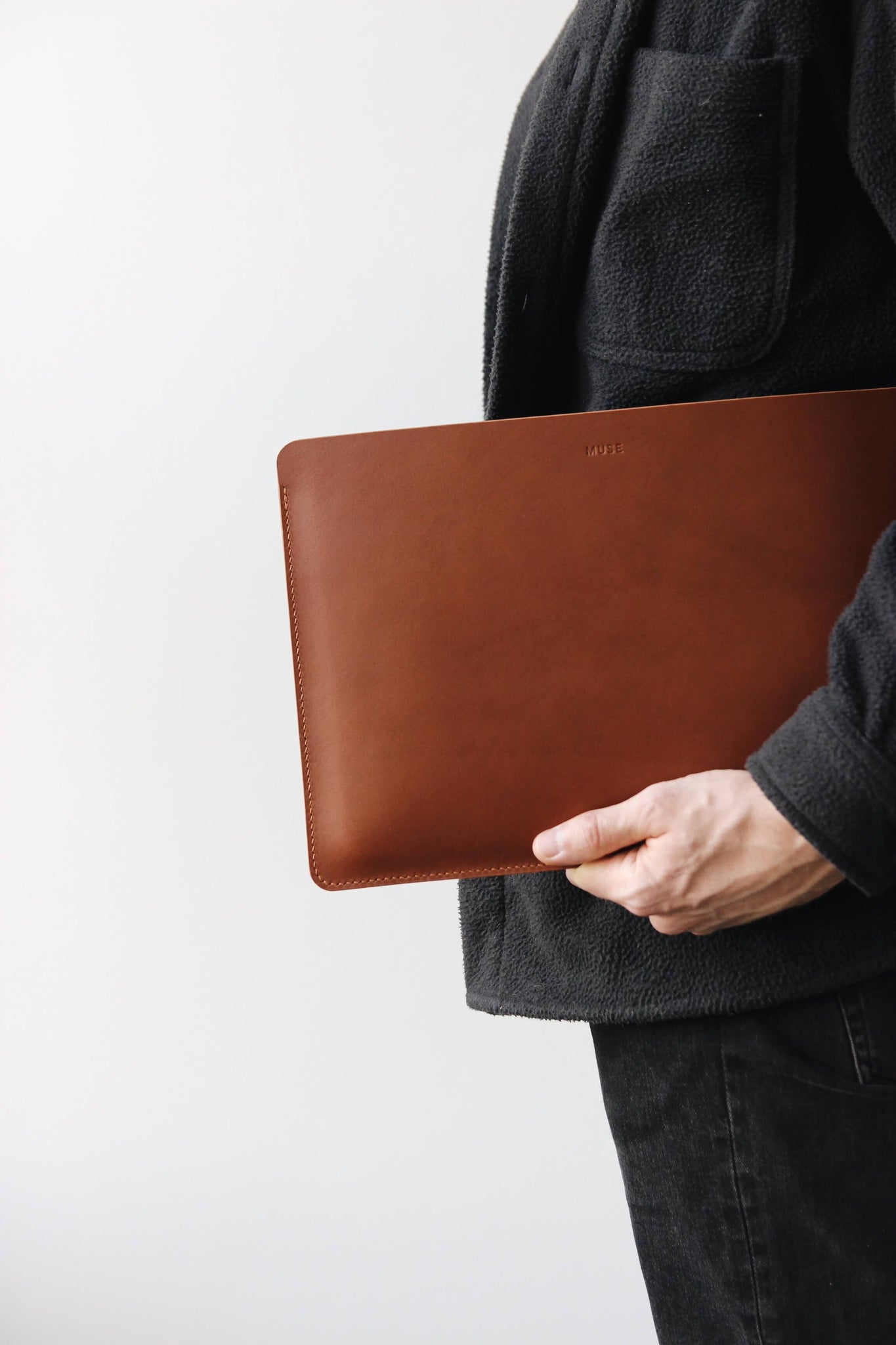 Eine Leder MacBook Hülle in Braun wird von jemandem in schwarzer Kleidung in der Hand gehalten.