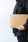 Eine Leder MacBook Hülle in Natural wird von jemandem in schwarzer Kleidung in der Hand gehalten.