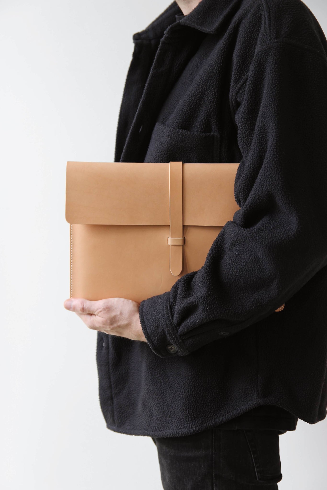 Ein schwarz gekleideter Mann hält eine MacBook Hülle aus Leder in Natural unter dem Arm.