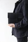 Ein schwarz gekleideter Mann hält eine MacBook Hülle aus Leder in Schwarz unter dem Arm.