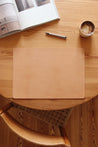 Auf einem Holztisch liegt eine Schreibtischunterlage aus Leder in Natural und als Dekoration eine Kaffeetasse, ein Stift und ein aufgeklapptes Buch.