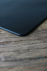 Nahaufnahme der Lederkante einer Leder MacBook Hülle in Schwarz auf einem Holztisch.