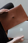 Ein MacBook wird in eine MacBook Hülle aus Leder in Braun geschoben.