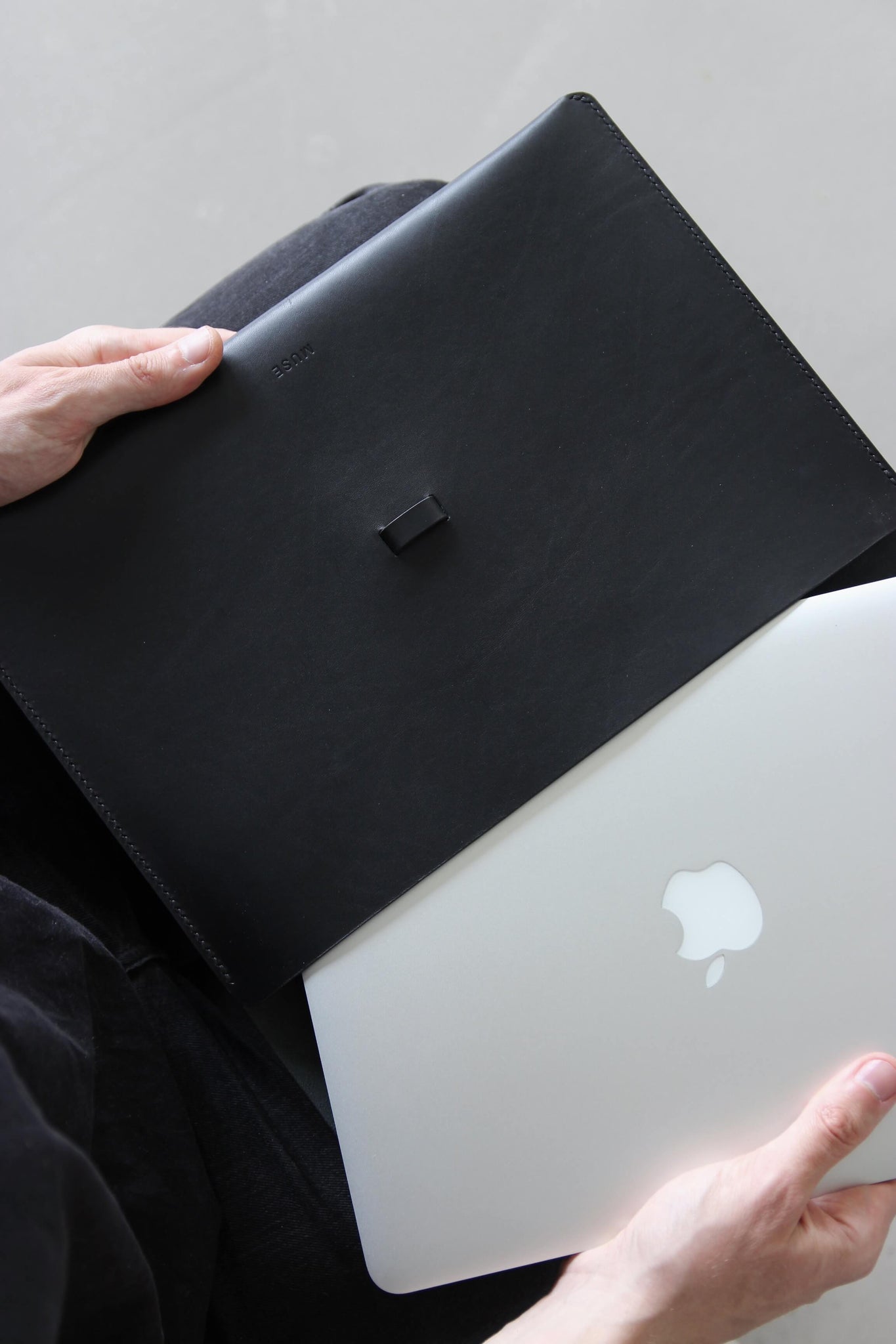 Ein MacBook wird in eine MacBook Hülle aus Leder in Schwarz geschoben.