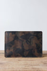 Eine Leder MacBook Hülle in Camo steht auf einem Holztisch.