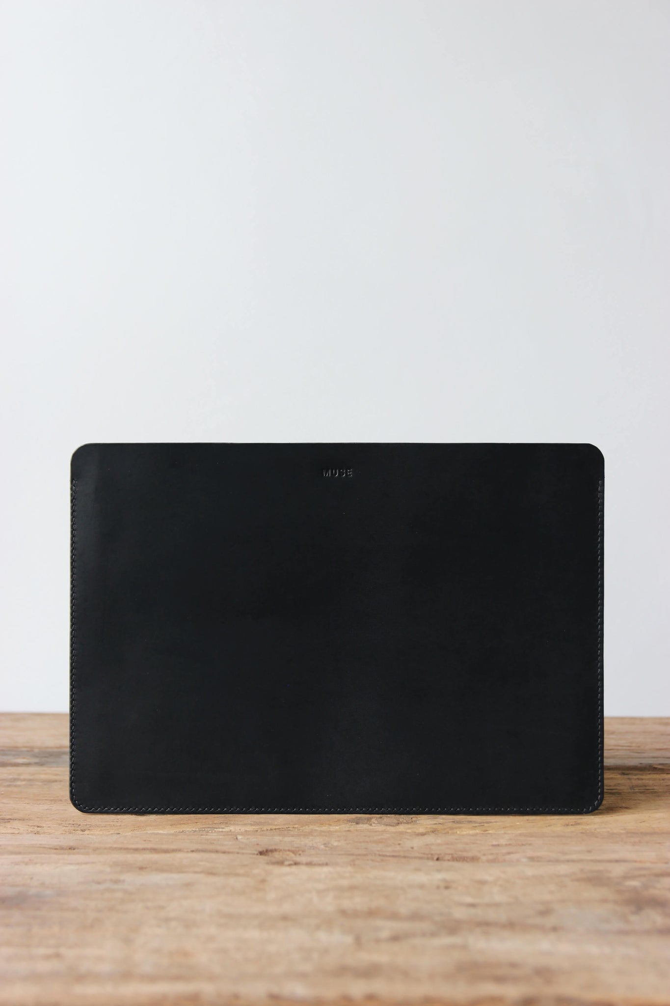 Eine Leder MacBook Hülle in Schwarz steht auf einem Holztisch.