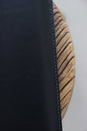 Detailaufnahme der Naht einer MacBook Hülle aus Leder in Schwarz auf einem Holzstuhl.