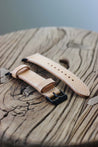 Seitenaufnahme eines Apple Watch Lederarmbands in Natural auf einem Holzhocker.