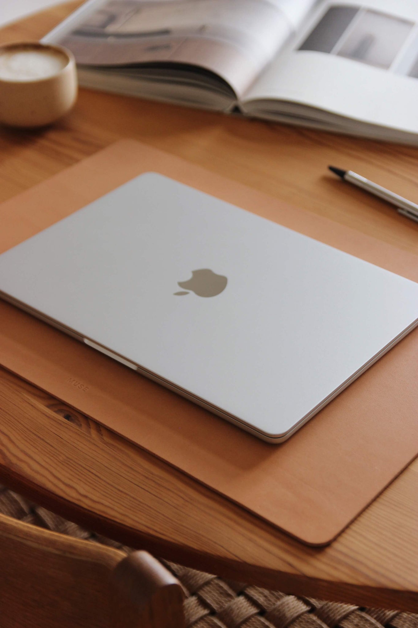 Seitenansicht einer Schreibtischunterlage aus Leder in Natural auf einem Holztisch und auf dieser befindet sich ein zugeklapptes MacBook.