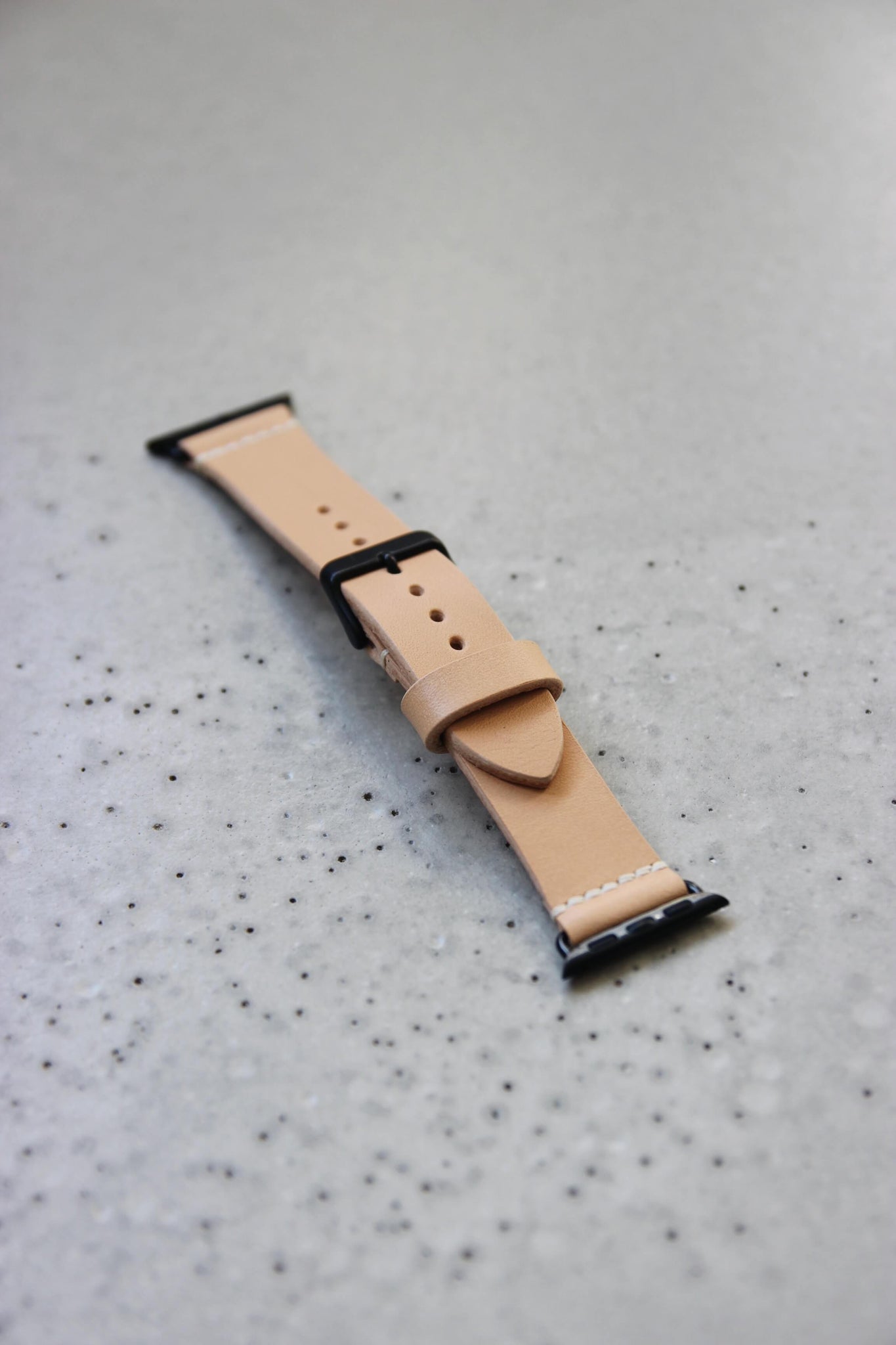 Apple Watch Lederband in Natural auf einem Betonboden liegend.