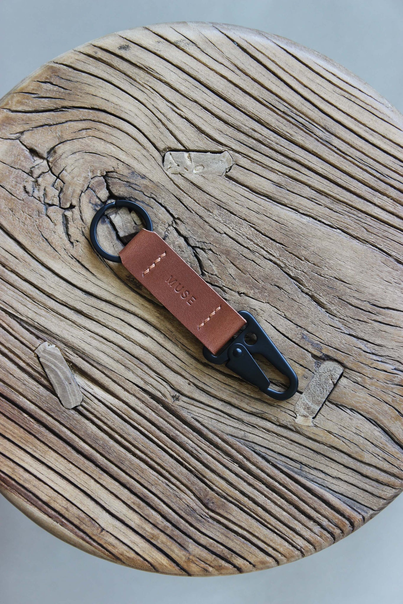 Ein Leder Schlüsselanhänger in Braun mit einem Karabiner und Schlüsselring in Schwarz auf einem Holzstuhl.