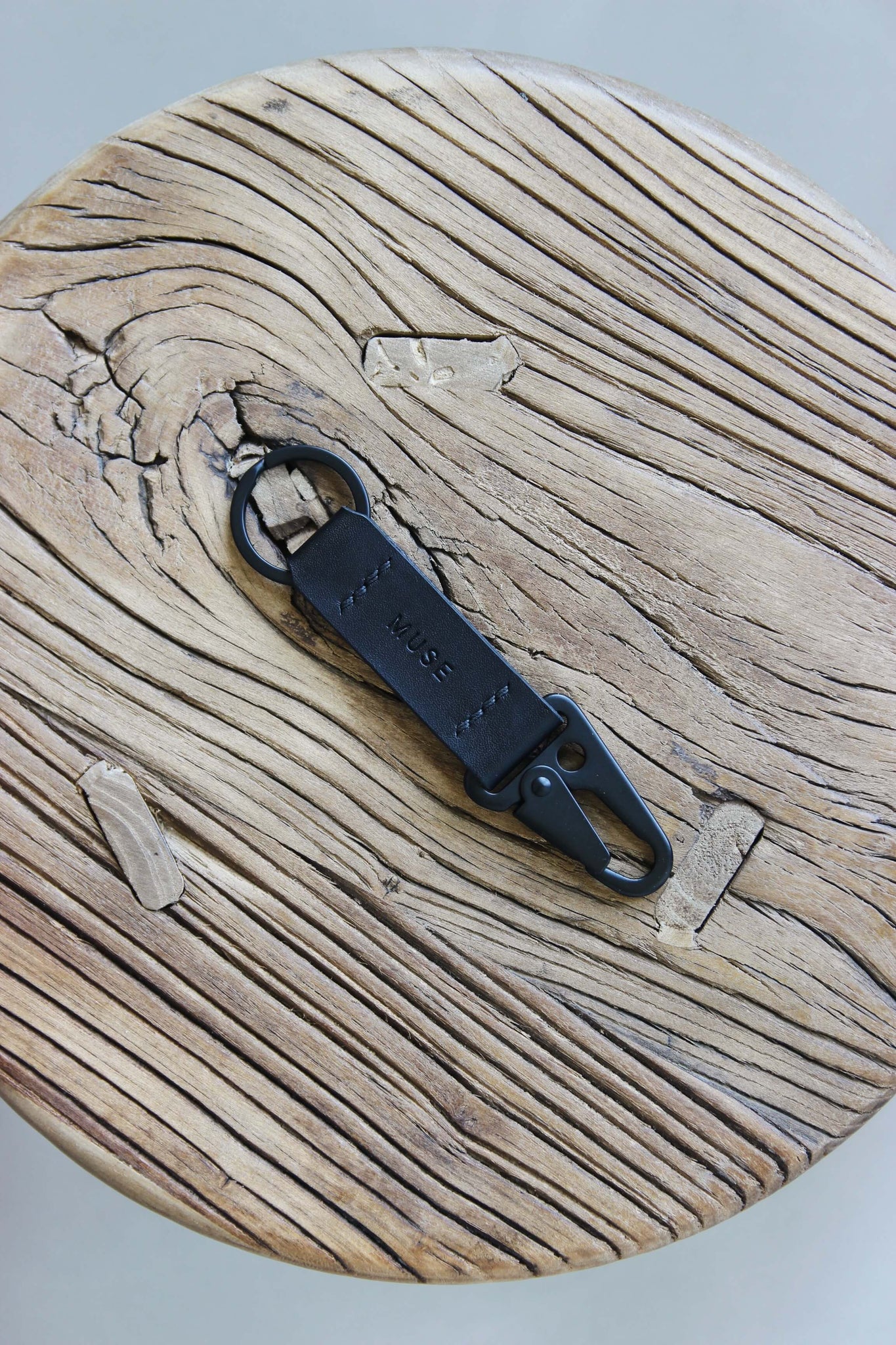 Ein Leder Schlüsselanhänger in Schwarz mit einem Karabiner und Schlüsselring in Schwarz auf einem Holzstuhl.