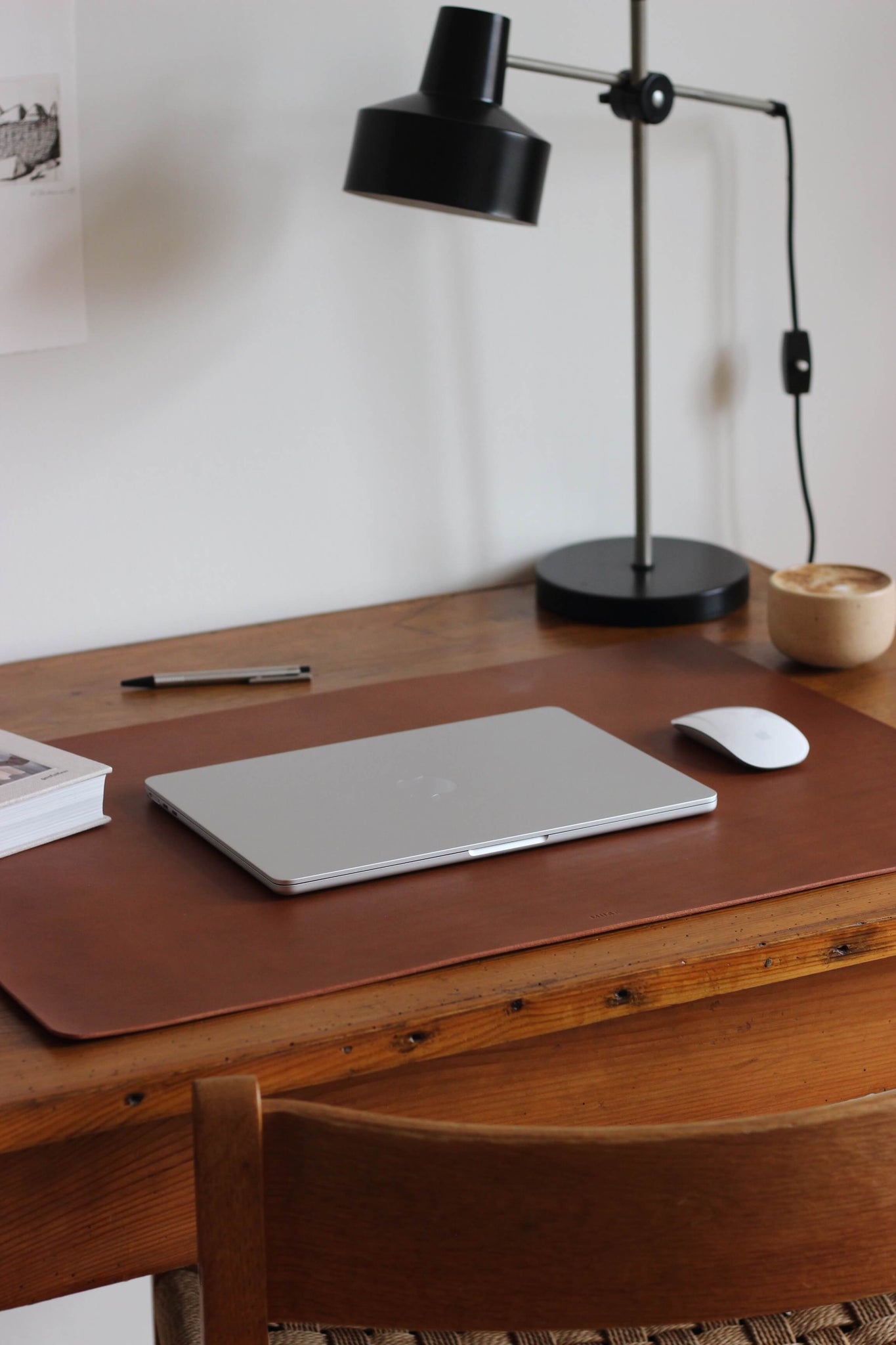 Seitliche Ansicht einer Leder Schreibtischunterlage in Braun auf einem Holzschreibtisch und darauf liegt ein zugeklapptes MacBook und eine Maus.