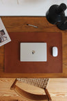 Leder Schreibtischunterlage in Braun auf einem Schreibtisch aus Holz und auf dieser befindet sich ein zugeklapptes MacBook und eine Maus.