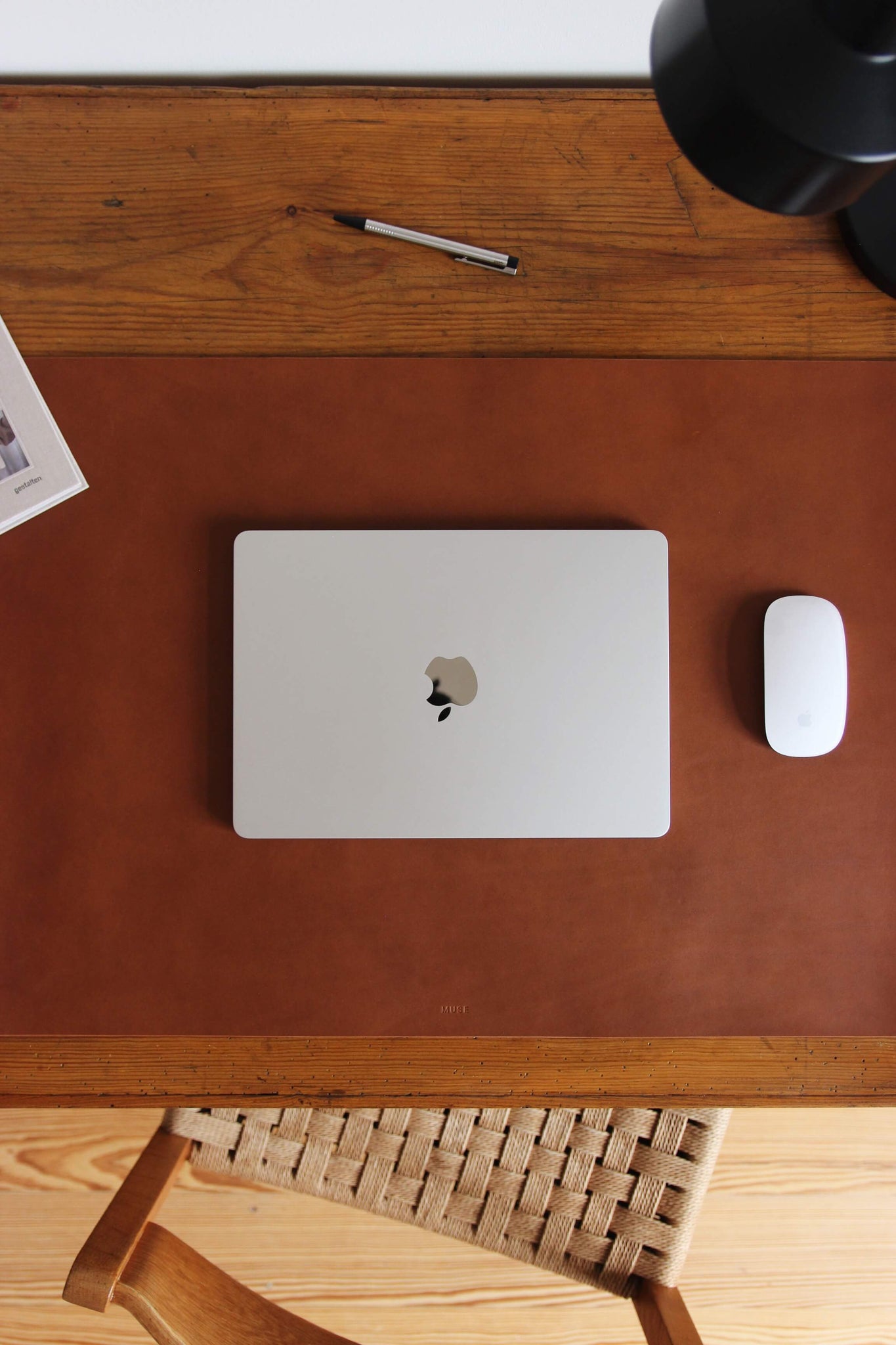 Nahaufnahme einer Leder Schreibtischunterlage in Braun auf einem Schreibtisch aus Holz und auf dieser liegt ein zugeklapptes MacBook und eine Maus.
