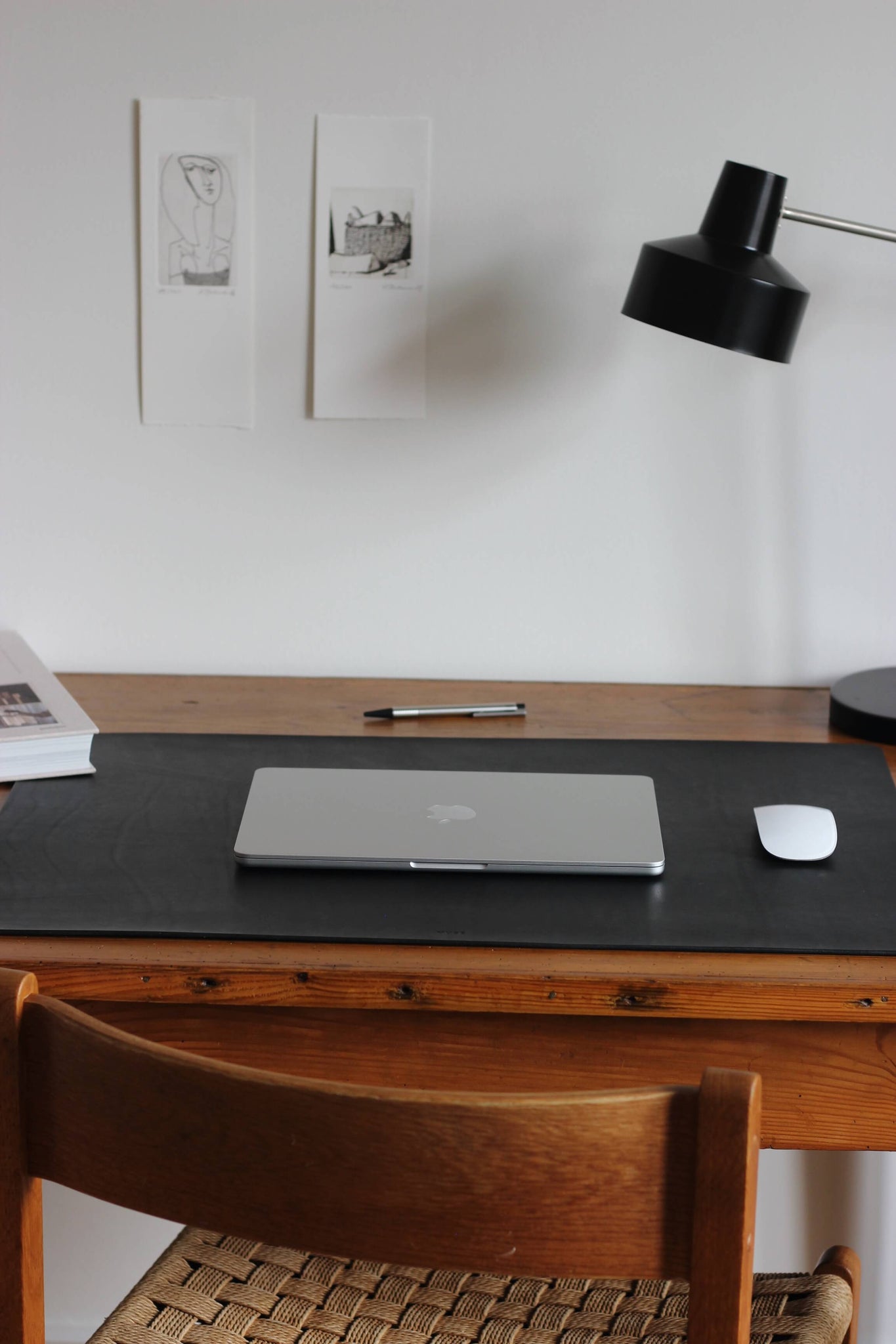 Eine Leder Schreibtischunterlage in Schwarz liegt auf einem Schreibtisch aus Holz und darauf befindet sich ein zugeklapptes MacBook und eine Maus.