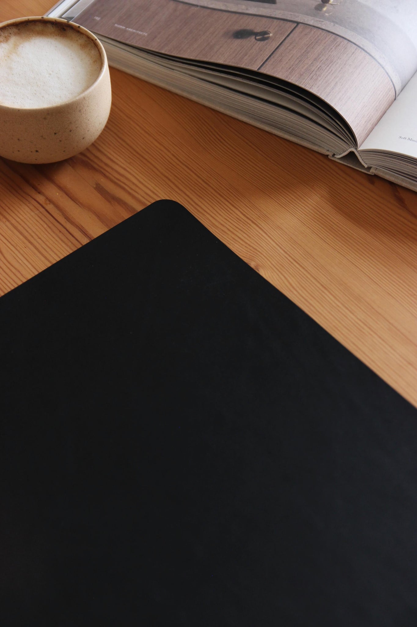 Lederkante einer Schreibtischunterlage aus Leder in Schwarz auf einer Holzplatte und eine Kaffeetasse und ein Buch.