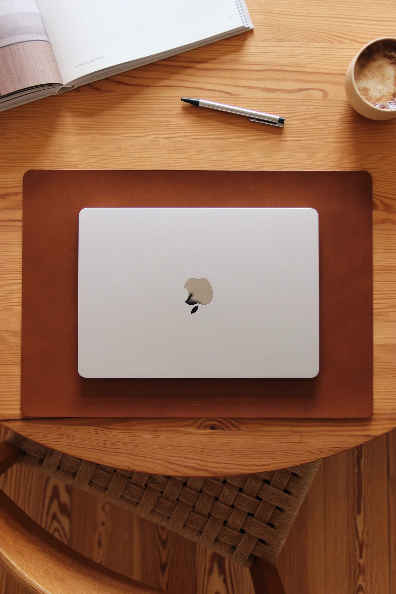 Auf einem Holztisch liegt einer Schreibtischunterlage aus Leder in Braun und auf dieser befindet sich ein zugeklapptes MacBook.