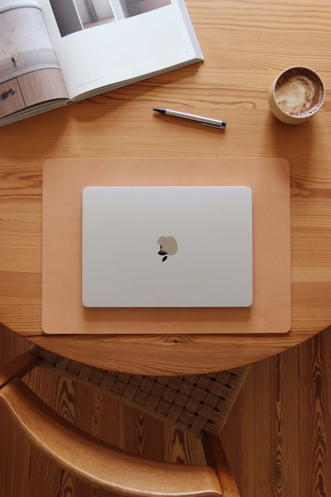 Eine Schreibtischunterlage aus Leder in Natural auf einem Holztisch und auf dieser befindet sich ein zugeklapptes MacBook.