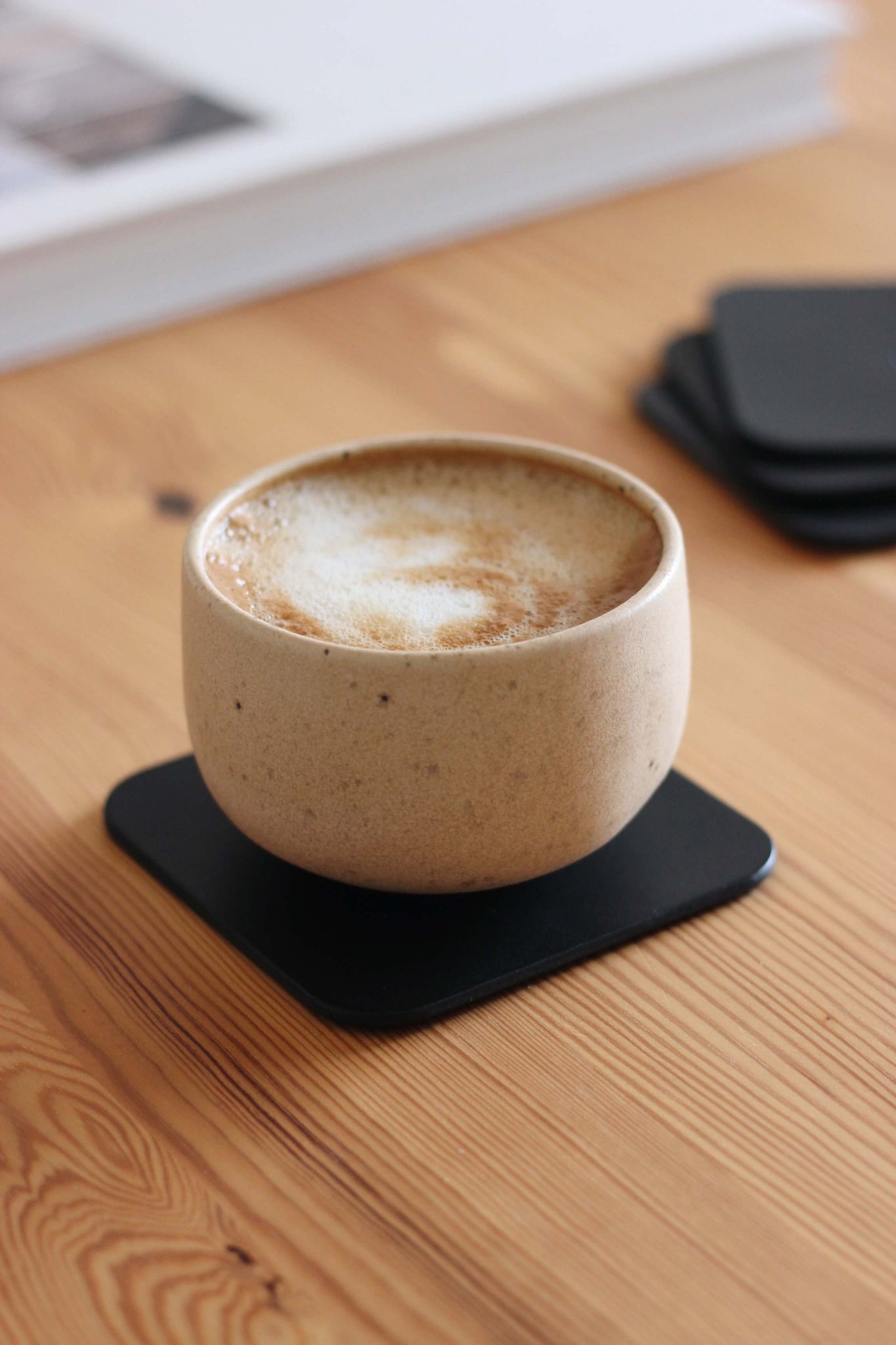 Eine Kaffeetasse steht auf einem Leder Untersetzer in Schwarz auf einem Holztisch.