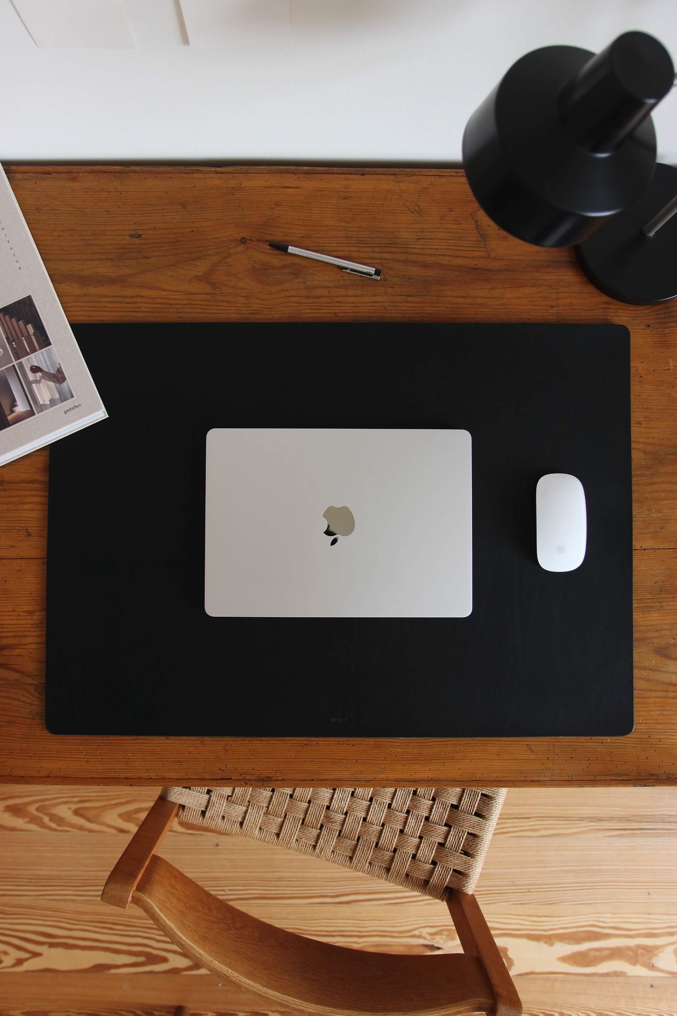 Leder Schreibtischunterlage in Schwarz auf einem Schreibtisch aus Holz und auf dieser befindet sich ein zugeklapptes MacBook und eine Maus.