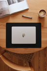 Eine Schreibtischunterlage aus Leder in Schwarz auf einem Holztisch und auf dieser befindet sich ein zugeklapptes MacBook.