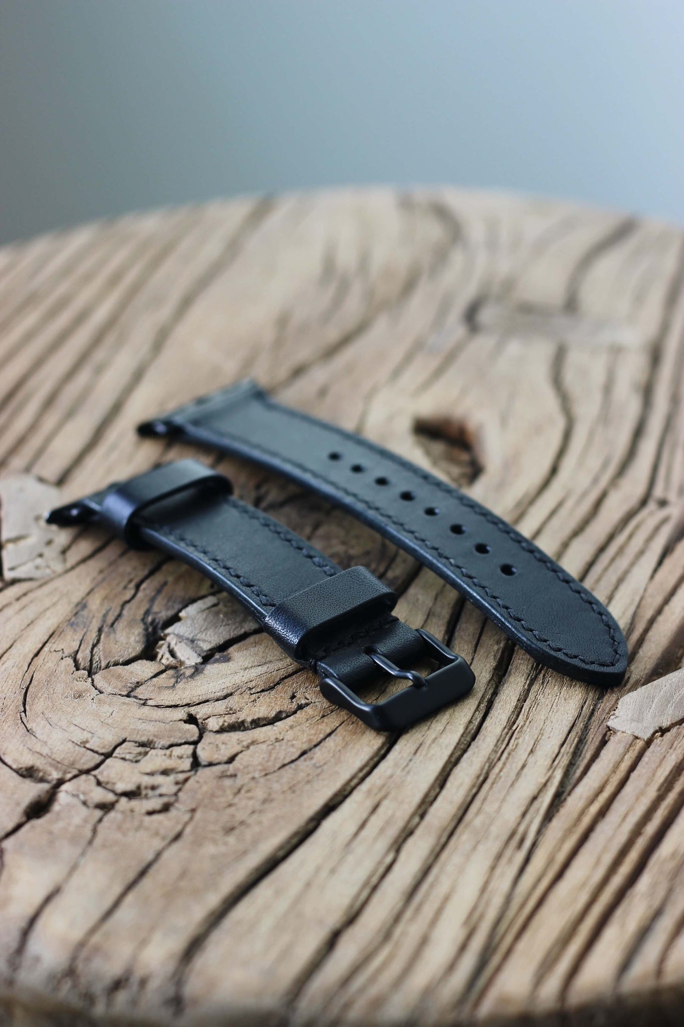Seitenaufnahme eines Apple Watch Lederarmbands in Schwarz auf einem Holzhocker.