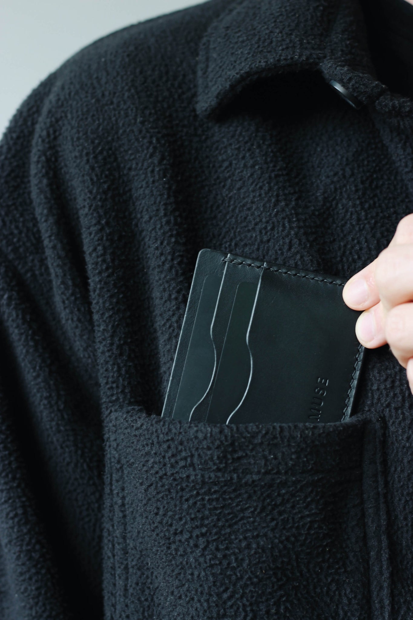 Kartenetui aus Leder in Schwarz wird in eine Brusttasche eines schwarzen Oberteils gesteckt.