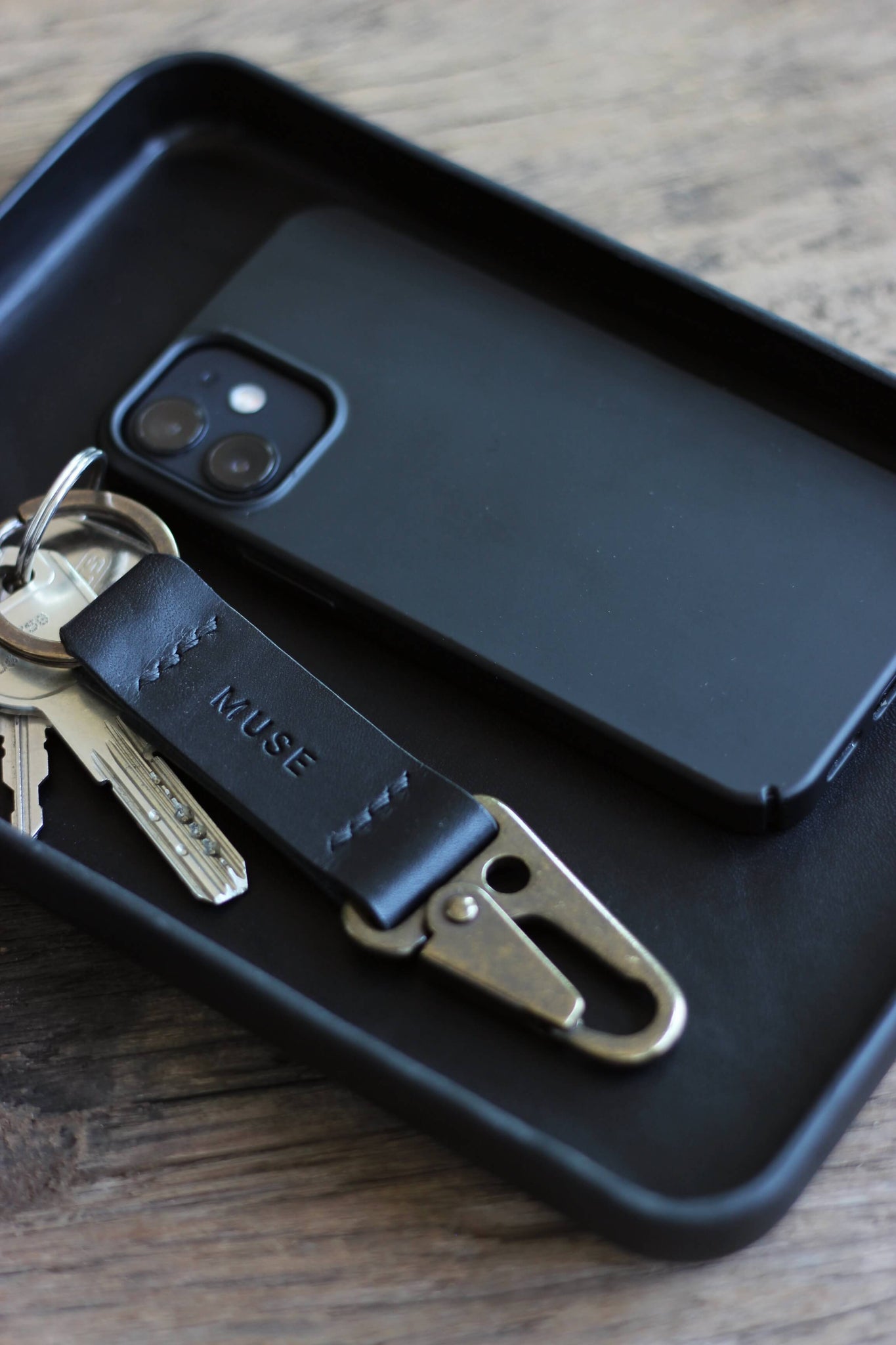 Nahaufnahme einer kleinen Ablageschale aus Leder in Schwarz und in dieser befindet sich ein Handy und ein Schlüsselanhänger.